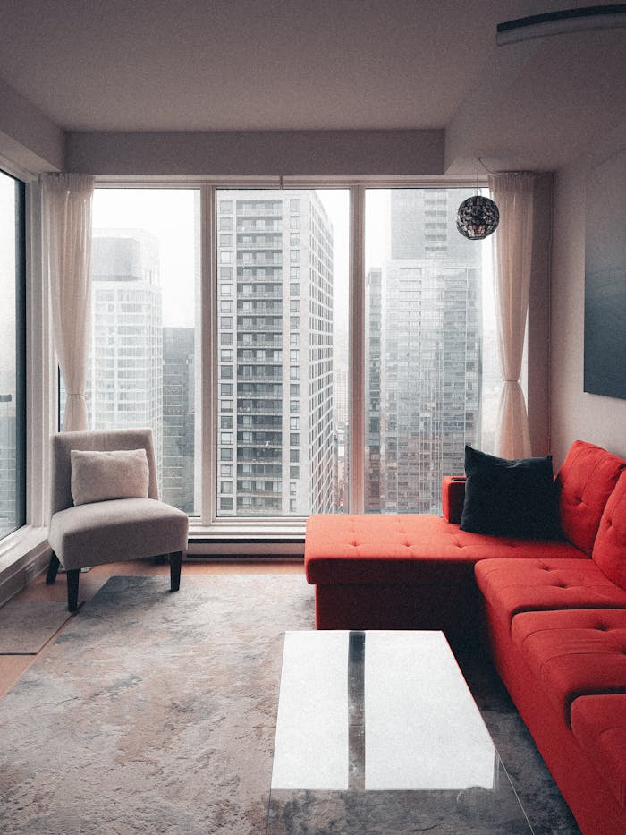 hero-02 Stylish living room featuring a red couch and city skyscraper view.